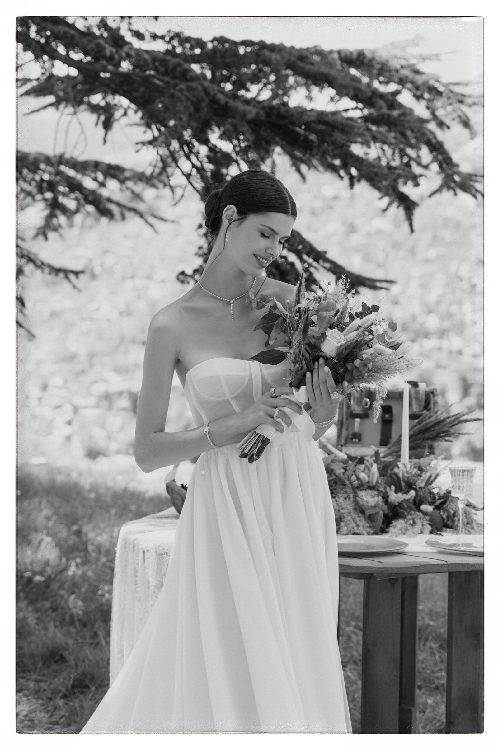 Black and white frame: the model holds a bouquet of dried flowers, her diamond drop necklace, bracelets and rings clear against the pale gown.