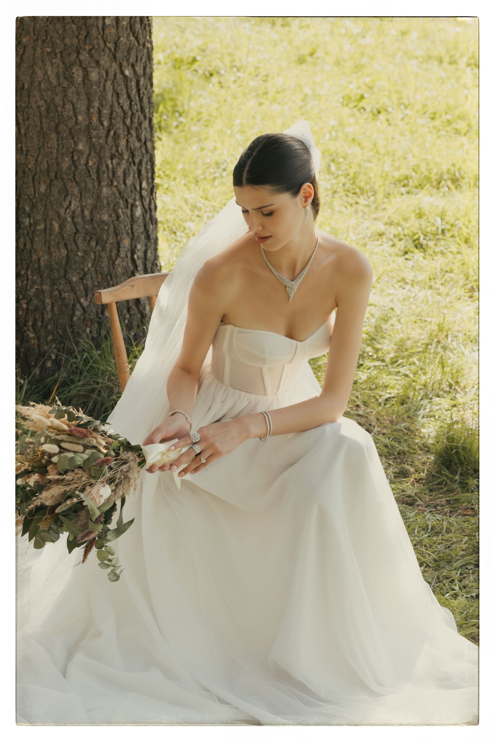 In a veil, head lowered over the bouquet in her lap, she wears a V-shaped diamond necklace, drop earrings, bracelets and a cluster ring.