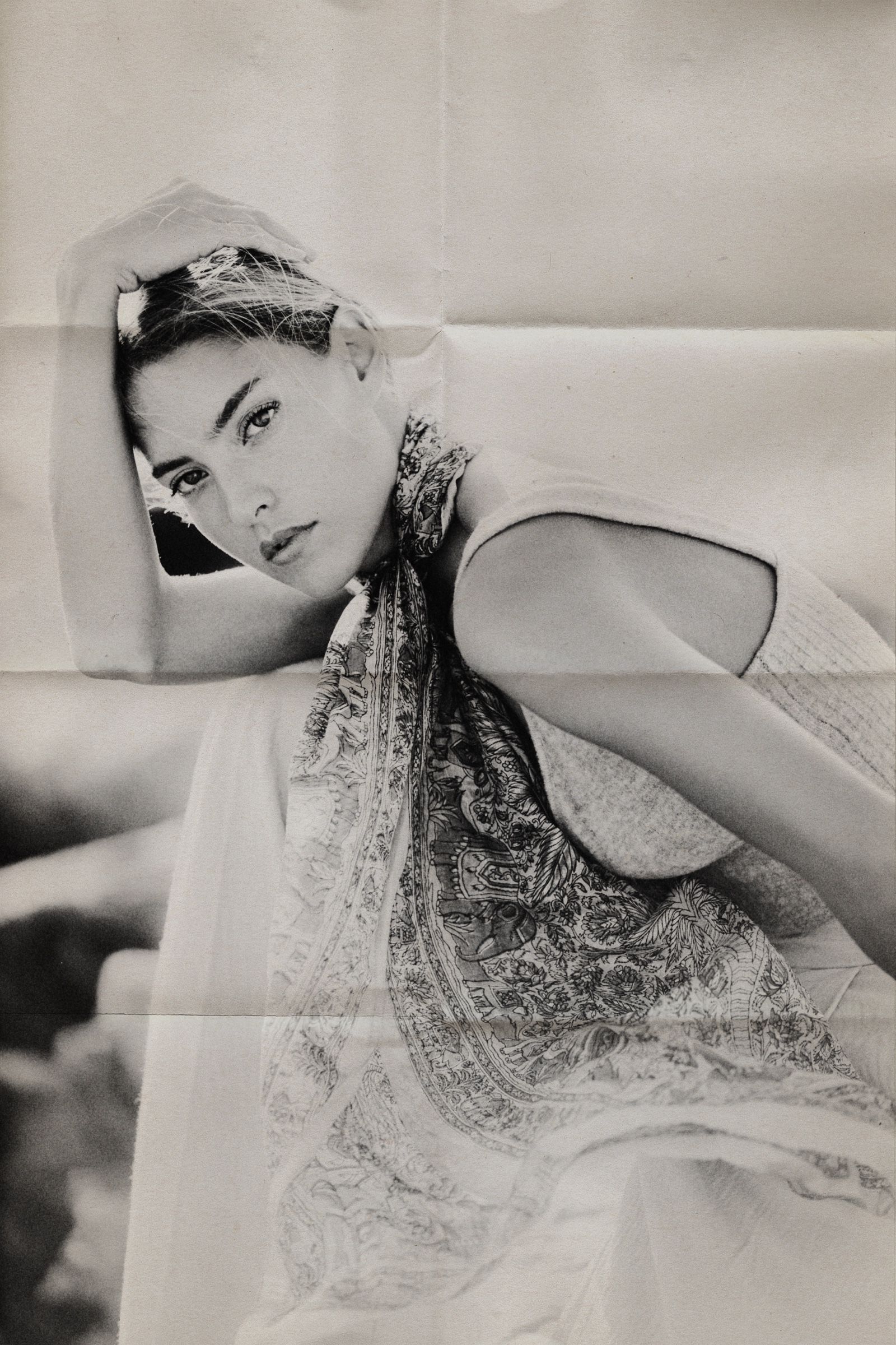 Toned monochrome on creased paper: Gio lies back with one arm over her head, the paisley scarf spread across her.