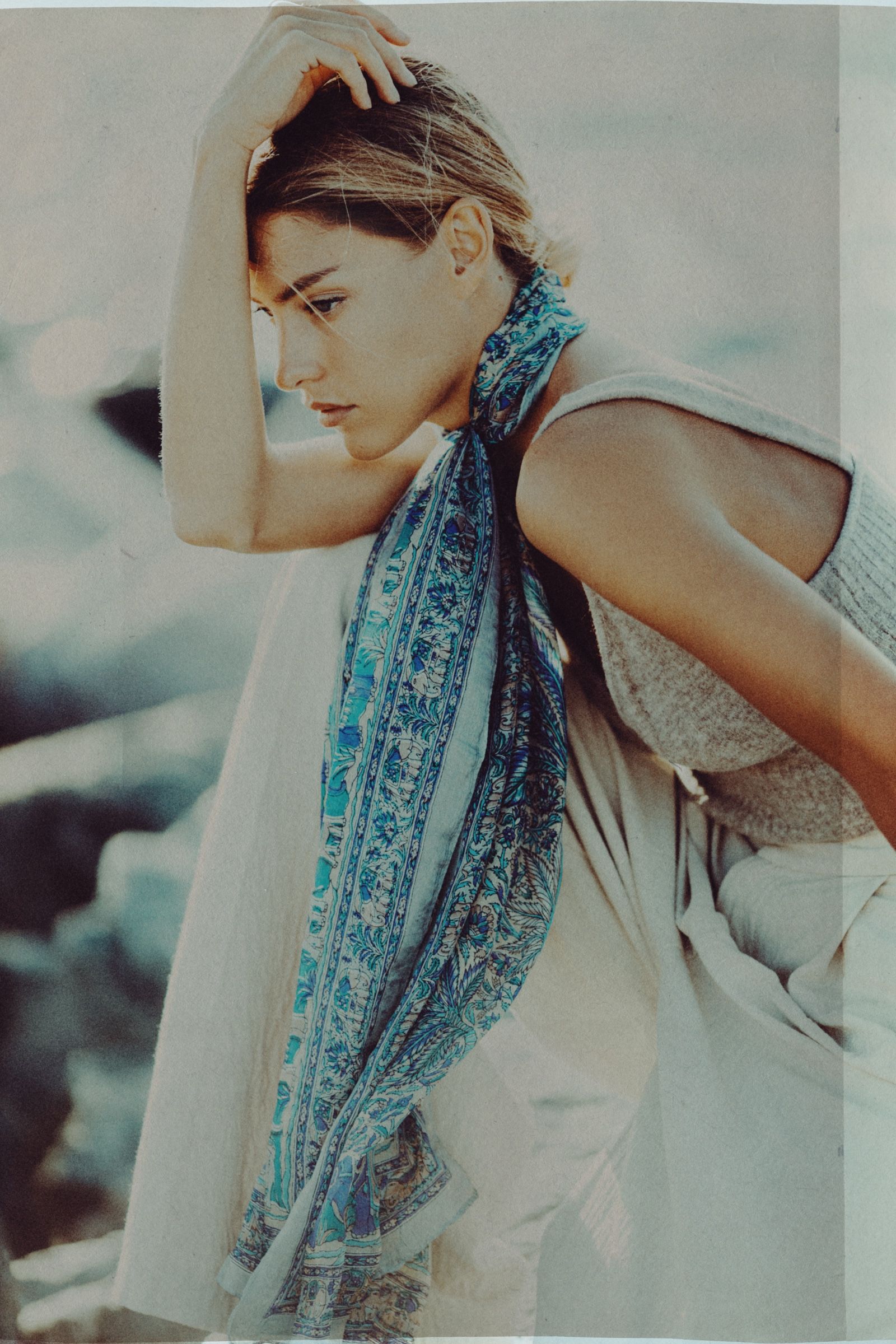 Turned in profile with one arm raised behind her head, the long paisley scarf running down the front of a pale linen shirt.