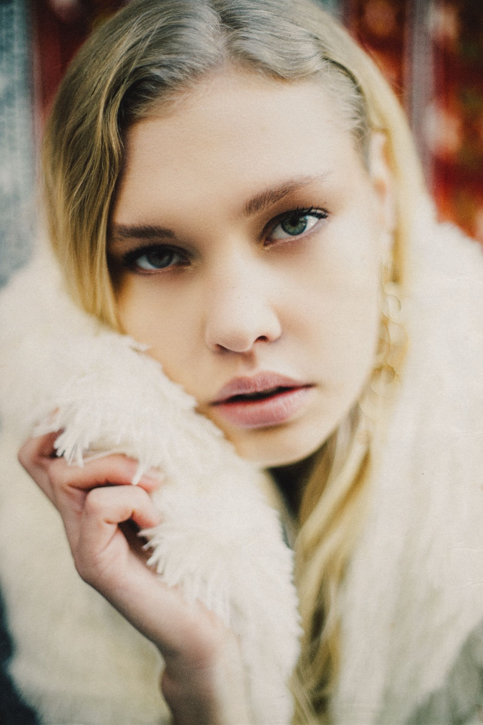Close portrait, the model's chin tucked into the white shaggy fur collar, one hand drawn up beside her face.