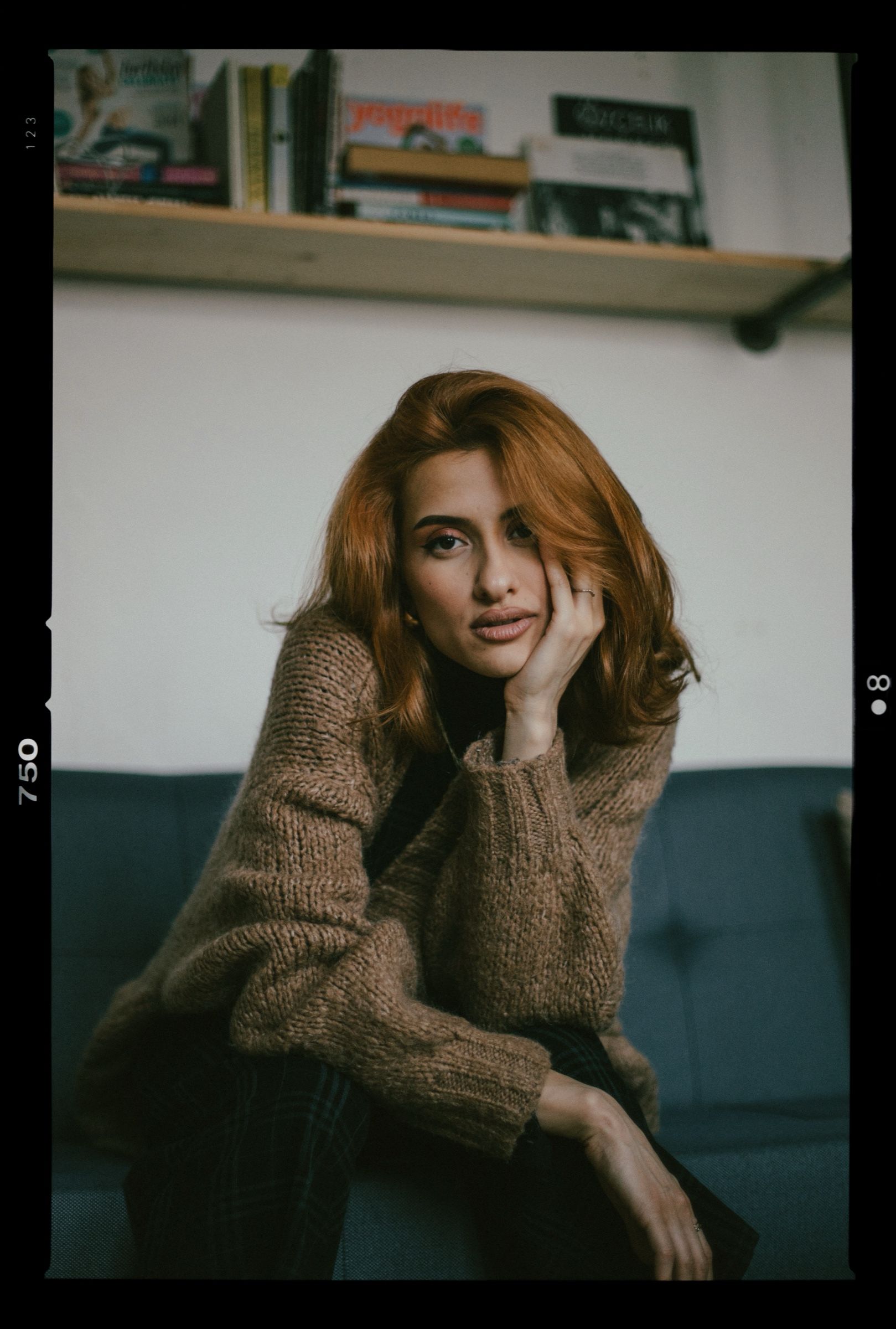 Elif rests her cheek on her hand on the blue sofa, the shot printed with its black film rebate and frame numbers.