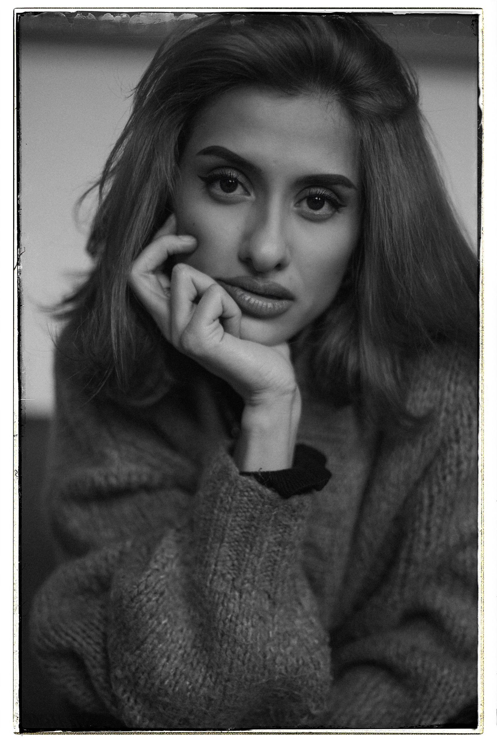 Elif in black and white, close in, both hands under her chin, looking level at the camera inside a dark film border.