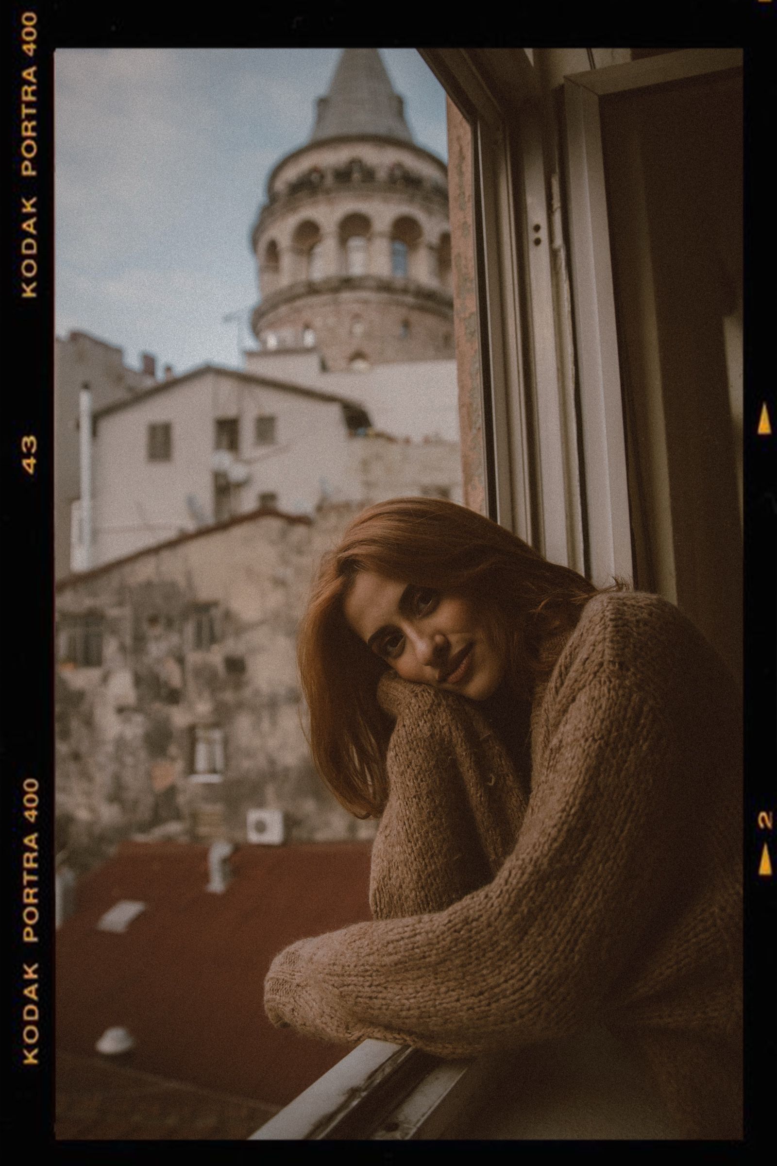Elif tilts her head onto her sleeve on the window ledge, the Galata Tower soft behind her, KODAK PORTRA 400 printed along the rebate.