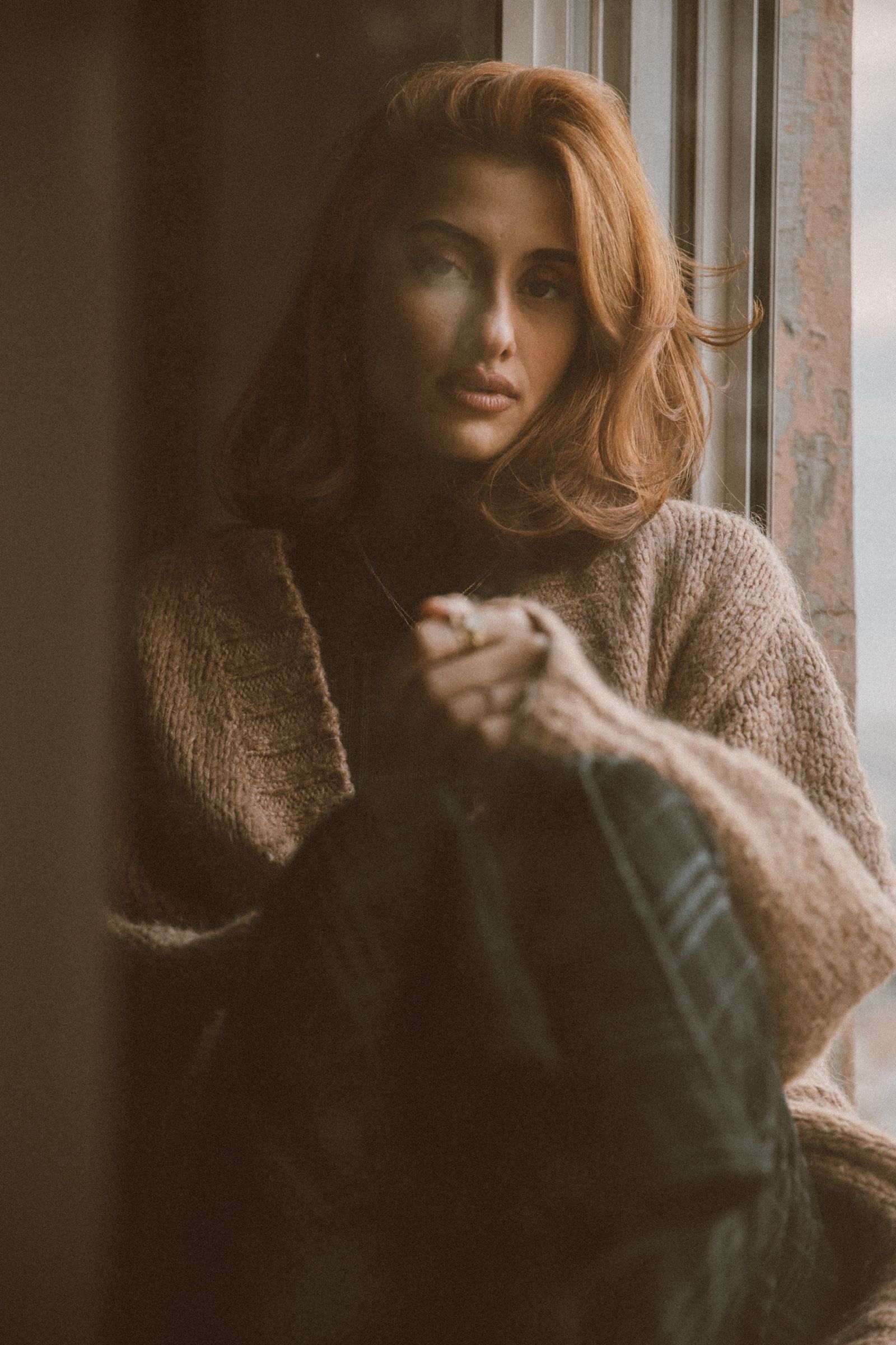 Elif turns toward the camera in the shadowed window, a lit cigarette in her hand, daylight catching the side of her face.