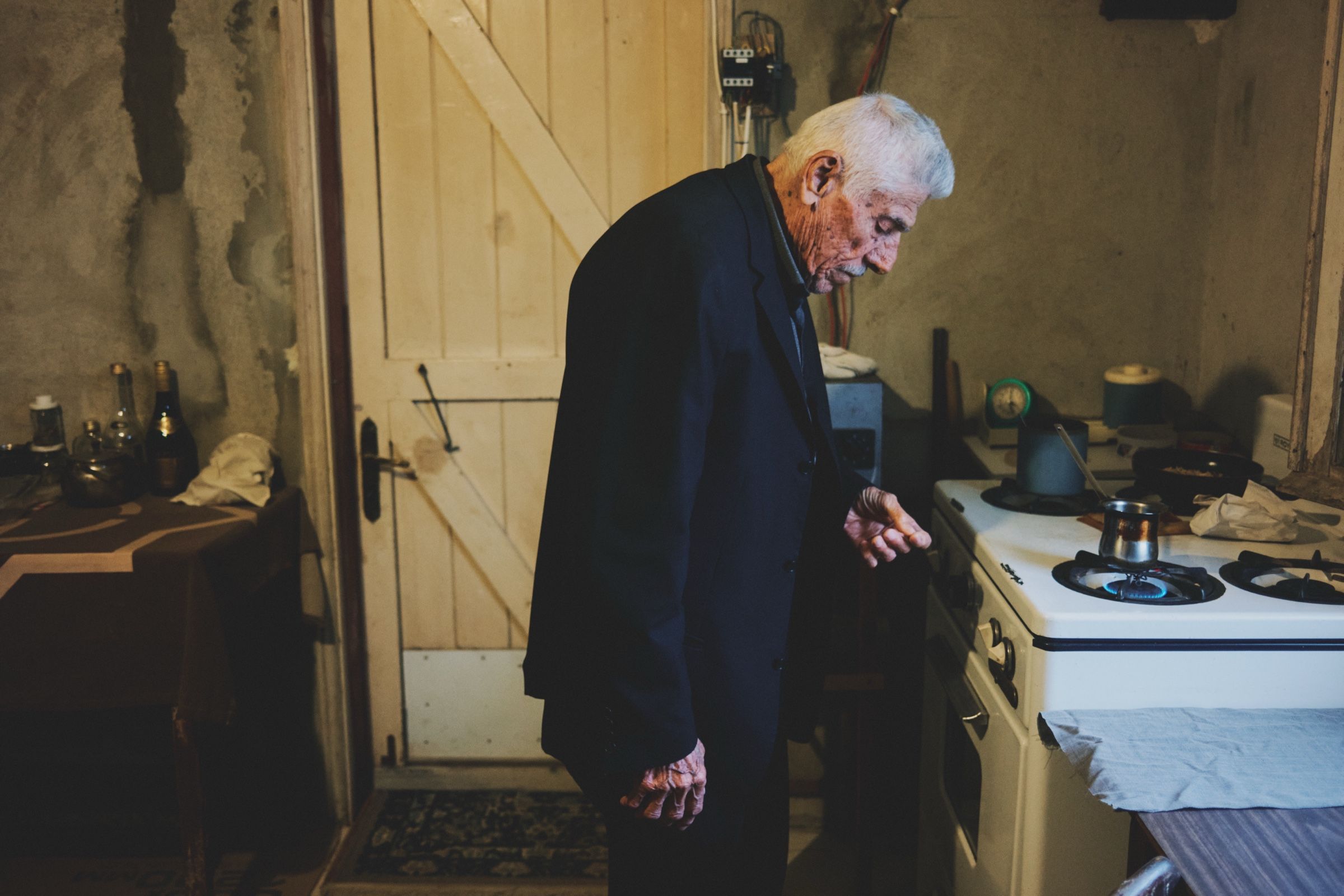 An old man, Youssef — 91, one of the oldest people in Joun — stands in his rusty kitchen, waiting for the Arabic coffee pot to boil. The town of Joun, Lebanon, 2025.