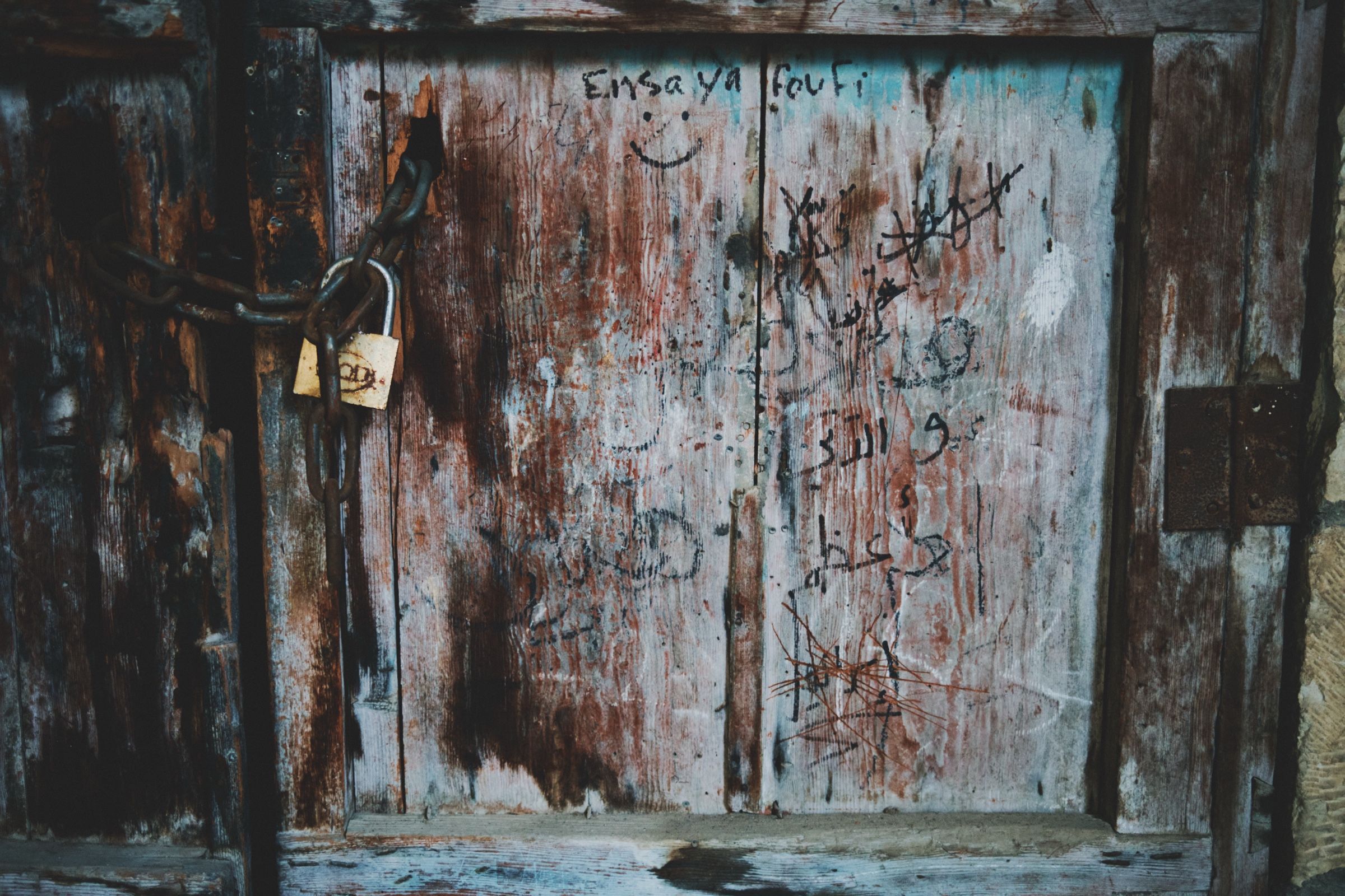 A locked wooden door in one of Joun’s old neighborhoods, its surface worn and covered with scribbles, and its rusted chains marking years of abandonment. The town of Joun, Lebanon, 2025.