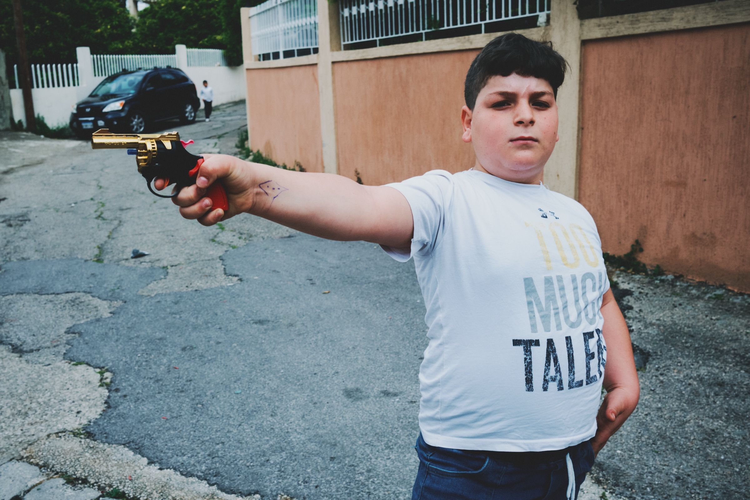 A boy points a toy gun while standing on a cracked street in Joun. The town of Joun, Lebanon, 2024.