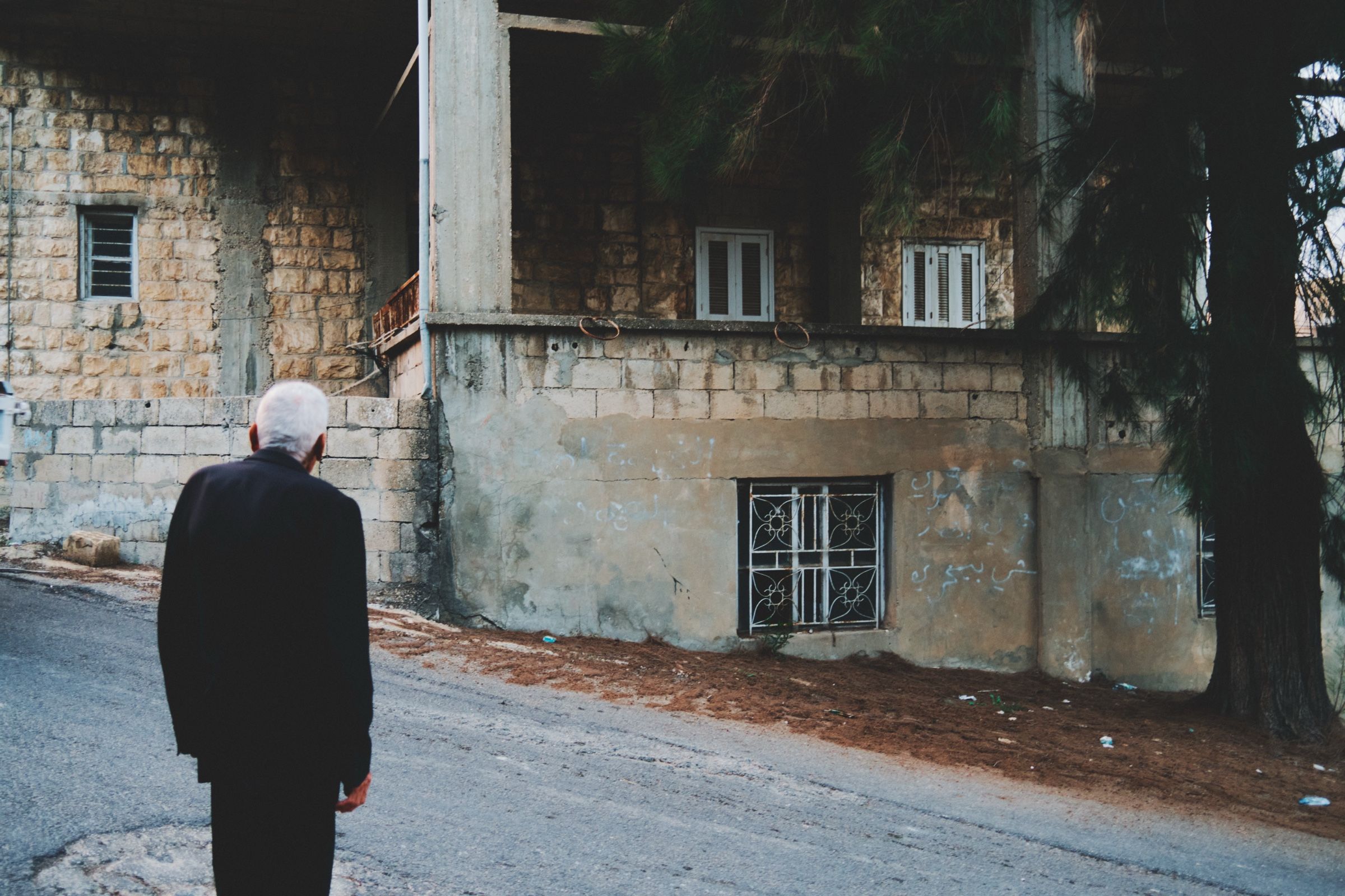 Youssef — 91, one of the oldest men in Joun — looks toward an abandoned house that once belonged to a close friend who left the village during the civil war. The town of Joun, Lebanon, 2025.
